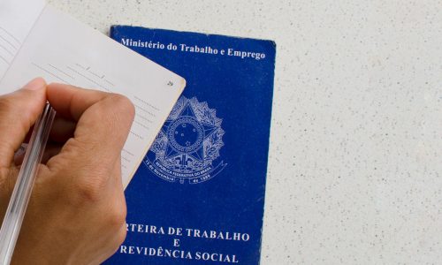 carteira de trabalho em mesa e pessoa escrevendo em outra carteira: advogado trabalhista em Santa Luzia